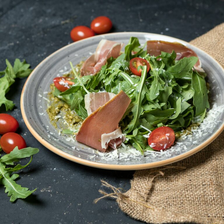 Fresh arugula salad topped with prosciutto, cherry tomatoes, and Parmesan cheese. Perfect for a gourmet meal.